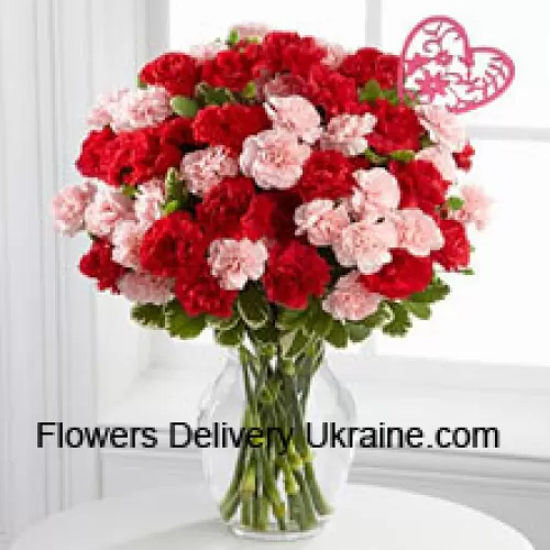 37 Oeillets (19 rouges et 18 roses) avec des remplissages saisonniers et un bâton en forme de cœur dans un vase en verre